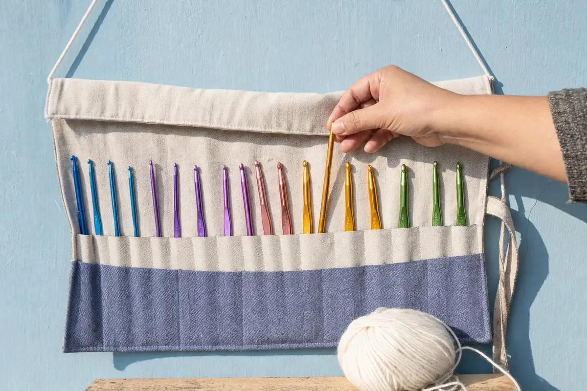 A hand takes a crochet hook from an unrolled hook case