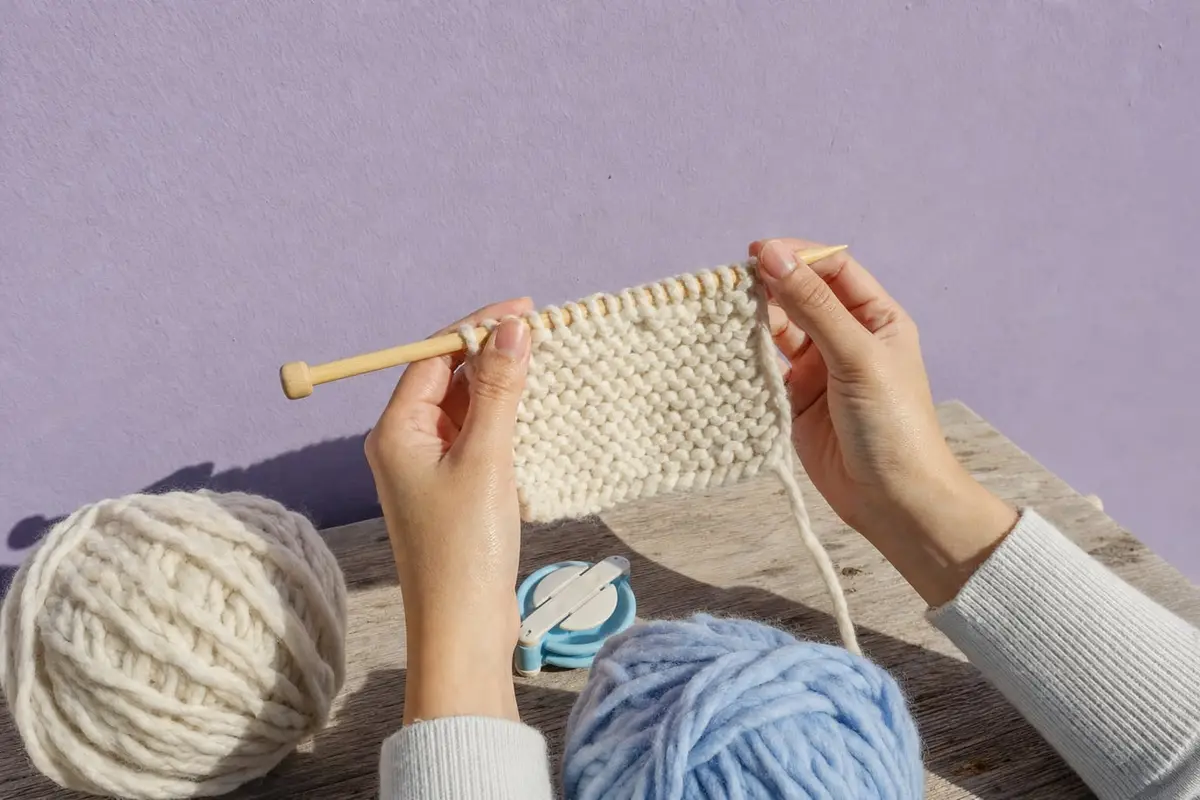 Hands hold a half-knit garter swatch above a beginner knitting kit