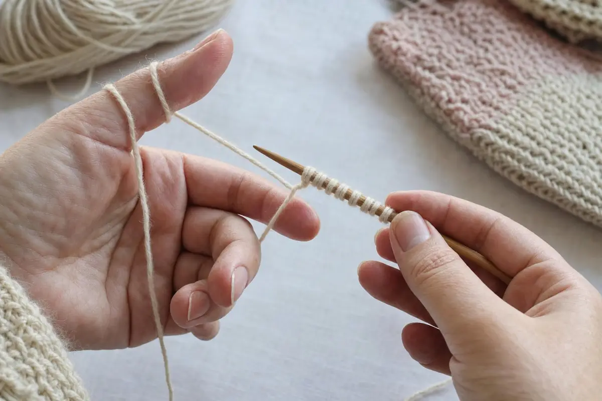 Hands make a long-tail cast-on on a bamboo knitting needle